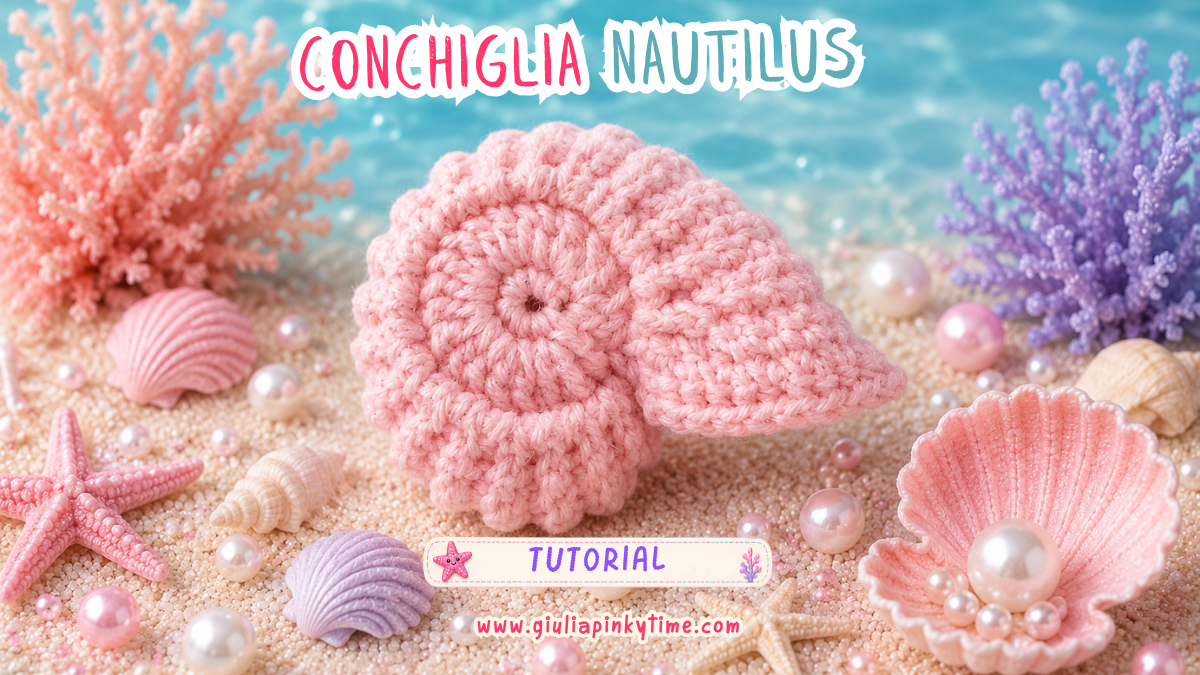 Conchiglia Nautilus all'uncinetto rosa realizzata a mano e appoggiata sulla sabbia in uno scenario marino decorato con coralli, stelle marine, conchiglie e perle nei colori pastello della collezione Pinky Summer Time.